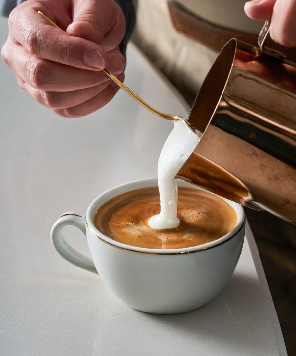 Close-up photo of a person preparing a cup of latte and coffee