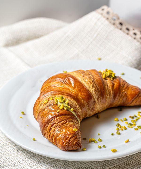Fresh croissant with pistachio topping on plate.